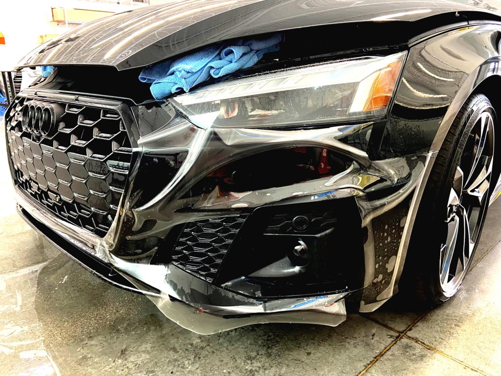 Paint protection film being laid over the front bumper of a black Audi at Mando Auto Film in Las Vegas
