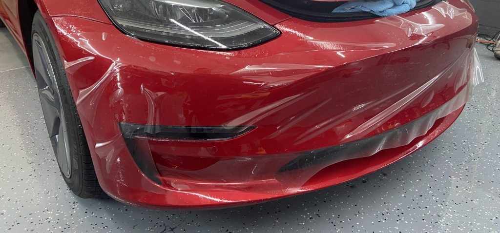 Paint protection film being applied to the front bumper of a red Tesla
